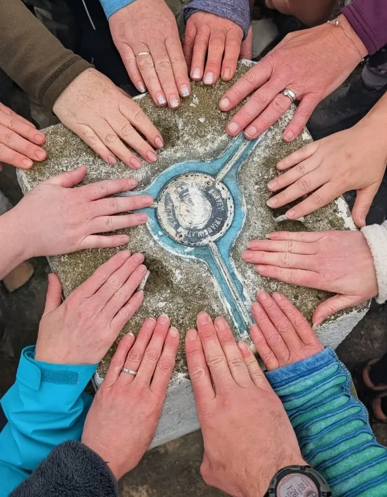 Walkers placing their hands together on a trig point